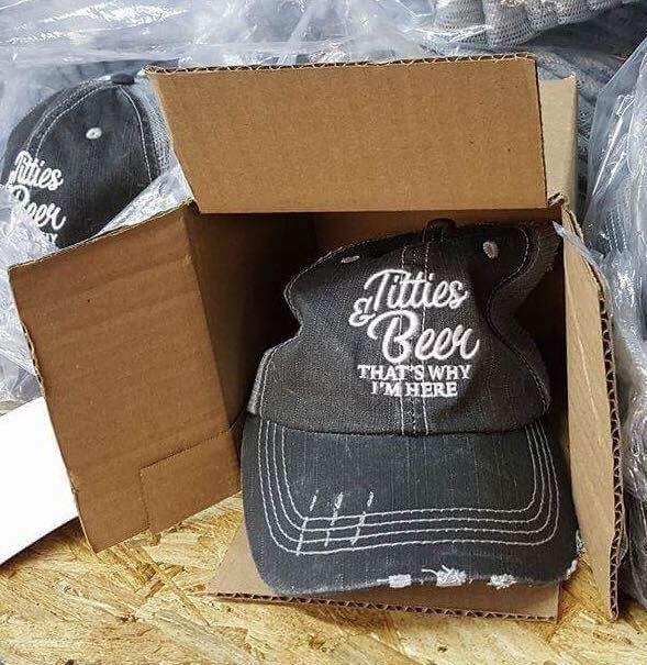 Schwarze Cap mit Spruch 'Titties & Beer' in Karton verpackt.