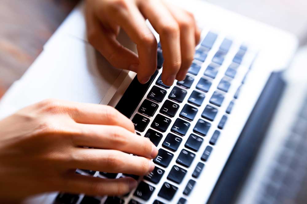 Nahaufnahme von Händen, die auf einer Laptop-Tastatur tippen.