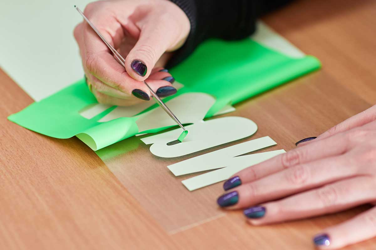 Person schneidet Buchstaben für Flexprints aus grünem Papier.