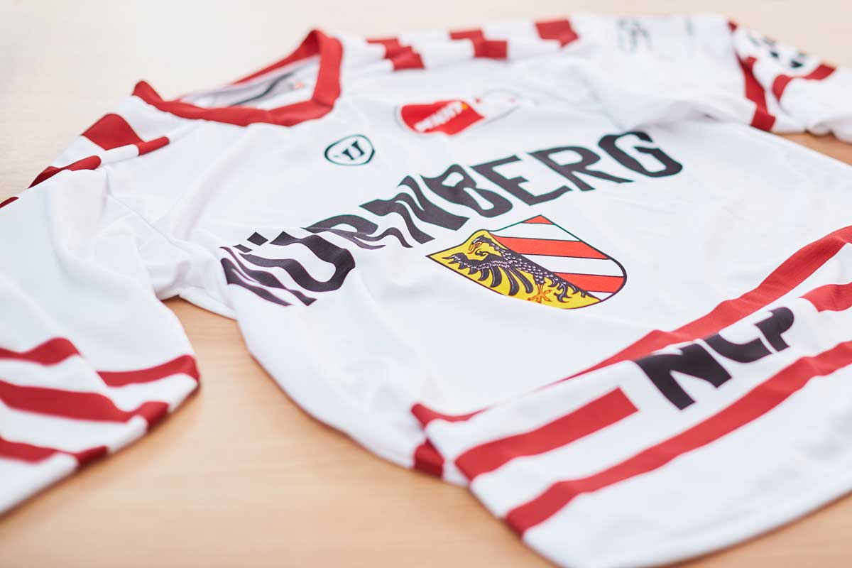 Weißes Fußballtrikot mit roten Streifen und Vereinswappen.